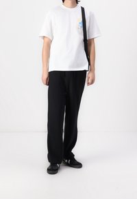 Vit bomullströja med ett blåt grafiskt tryck på bröstet, i kombination med svarta ribbade byxor och svarta sneakers. En svart axelväska hängande över axeln.