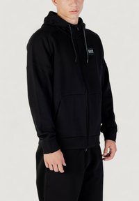 Schwarze Zip-Hoodie mit Kapuze, aus Jersey-Material, mit Vordertasche, gerippten Bündchen und einem kleinen Markenlabel auf der Brust.