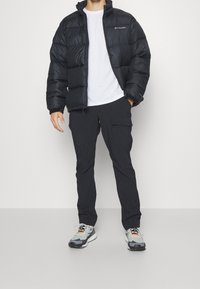 Černá prošívaná bunda se zipem, bílý tričko, tmavé cargo kalhoty a šedé tenisky s barevnými akcenty. Hladká tkanina, volný střih.