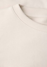 Sweatshirt beige clair avec un col rond côtelé et une texture lisse. La vue rapprochée met en évidence les détails du tissu et les coutures.