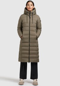 Olive green puffer coat with a hood, front zipper, and side pockets. Features a quilted design and a long silhouette. Paired with black pants and beige shoes.