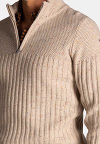 Beige gebreid pullover met een halve rits kraag, met ribbelstructuur en kleurrijke spikkels door de stof. Verstevigd met een gladde bovenkant.