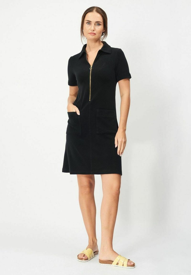 Svart klänning med dragkedja fram, korta ärmar, två framfickor och krage. Buren med gula sandaler som har ett vävt remdesign.