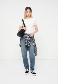 Υπερμεγέθεις μπλε τζιν, λευκή εφαρμοστή μπλούζα, μαύρη τσάντα κρεμασμένη στον ώμο και πουκάμισο σε καρό δεμένο στη μέση. Μαύρα και λευκά αθλητικά παπούτσια.