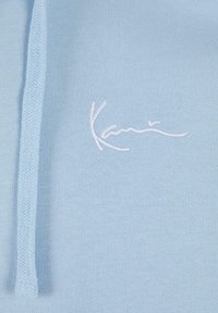 Helles blaues Kapuzenshirt aus weichem Stoff, mit einem strukturierten Kordelzug und einem weißen gestickten Logo auf der Brust.