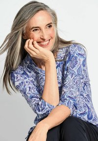 Bluse mit Muster in Blau und drei Viertelärmeln, versehen mit Wirbeln und floralen Designs in dunklerem Blau auf einem hellen Hintergrund. Weicher Stoff.