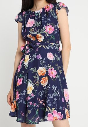 Vestido azul marino con flores rosas, naranjas y amarillas, mangas cortas y cinturón atado a la cintura, en una persona de pie.