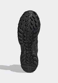 Semelle de chaussure de sport noire avec caoutchouc texturé pour l'adhérence, dotée d'un design structuré et d'un motif de crampons prononcé pour la stabilité.