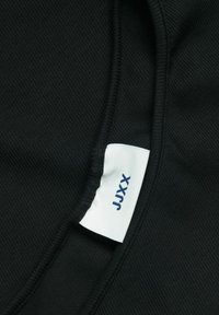 Tessuto a coste nero con una texture liscia. Presenta un'etichetta con la scritta "JXX" in blu navy. Il design include bordi curvi.