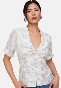 Floral button-up blouse in a light cream fabric with purple and blue patterns. Features short ruffled sleeves and a large collar.