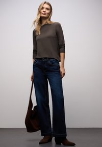 Lässiges Outfit mit einem enganliegenden, langärmligen dunklen Oberteil und weit geschnittenen dunkelblauen Jeans. Accessoires sind eine braune Schultertasche und braune Stiefel.