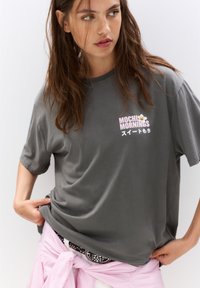 T-shirt en coton gris avec le texte "Mochi Mornings" en rose et blanc, col rond, coupe décontractée et manches courtes.
