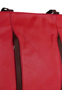 Rode synthetische draagtas met een gladde textuur, bruine leren accenten en contrasterende stiksels. Heeft een eenvoudig ontwerp met een ritssluiting bovenaan.