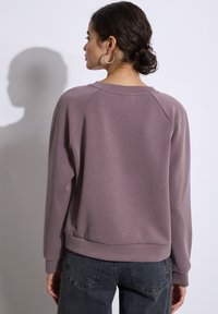 Felpa viola chiaro con design a raglan, polsini a coste e scollatura ampia. Tessuto morbido con una superficie liscia e vestibilità comoda.