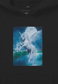 Sudadera negra con un gráfico de unicornio azul y blanco con alas, situado contra un fondo iluminado por la luna con acentos verdes.
