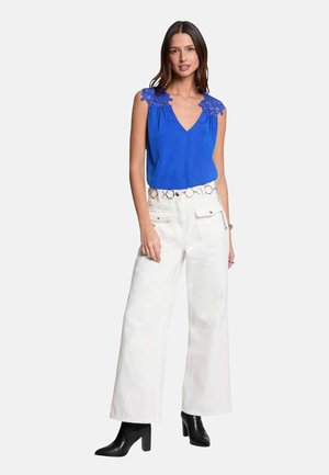 Top sin mangas de color azul real con detalles de encaje en los hombros, combinado con pantalones de pierna ancha blancos de tiro alto y botas negras hasta el tobillo.