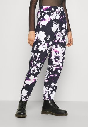 Zwart-witte tie-dye broek met bloemenprint, gedragen met zwarte veterlaarzen en een doorschijnende zwarte top met lange mouwen, weergegeven vanaf de taille naar beneden.