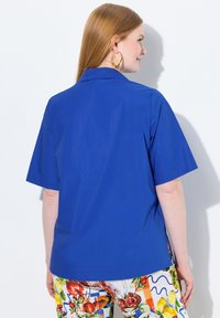 Camicia azzurra a maniche corte con colletto, realizzata in tessuto morbido. Indossata con pantaloni floreali a fantasia dai colori vivaci e dai design accattivanti.