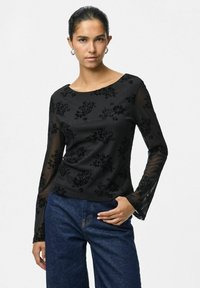 Top nero a maniche lunghe con motivo floreale in velluto, maniche trasparenti e scollatura rotonda, abbinato a pantaloni in denim scuro.