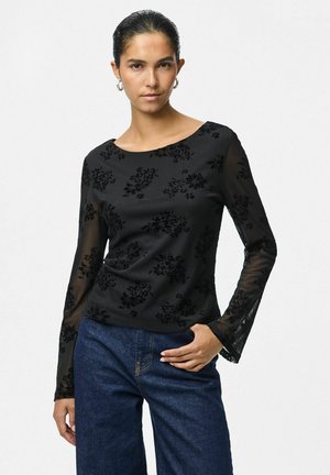 Haut noir à manches longues avec un motif floral en velours, manches transparentes et encolure ronde, associé à un pantalon en denim foncé.