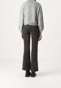 Šedý pletený svetr s texturovaným povrchem, doplněný tmavě zelenými zvonovými manšestrovými kalhotami. Černé silné podpatky outfit doplňují.