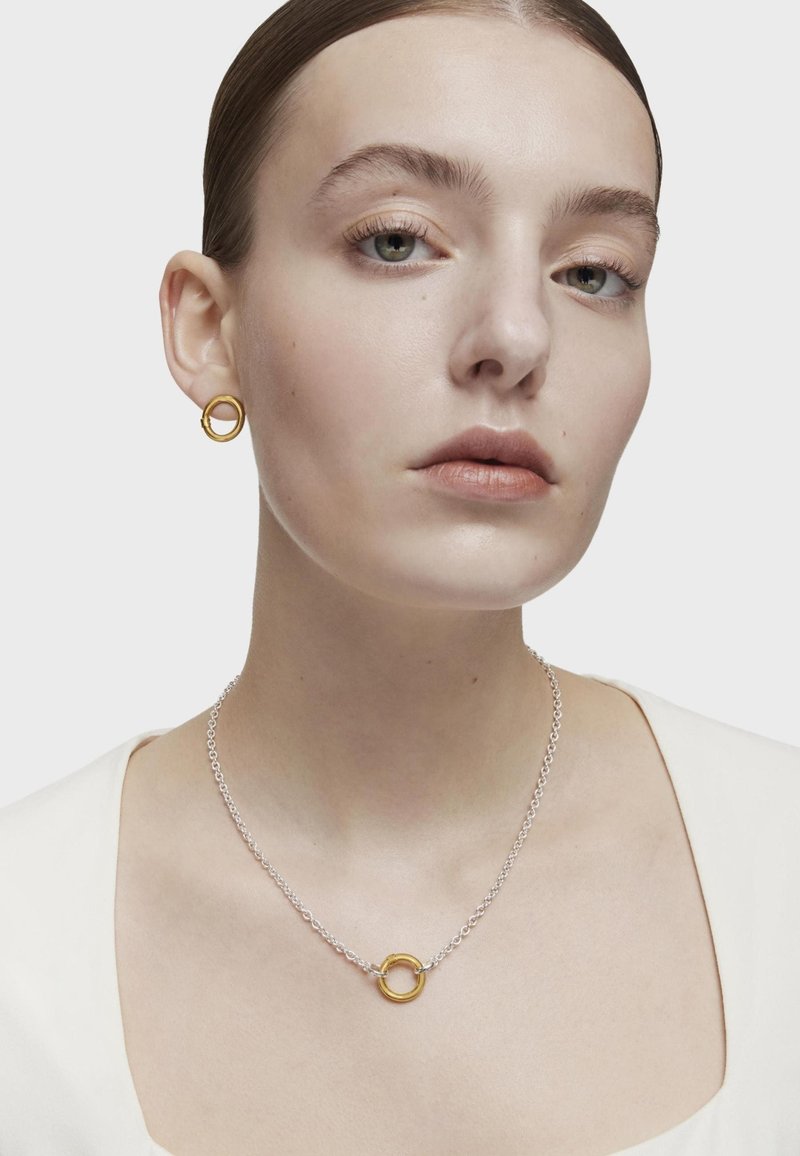 Pendientes circulares de oro y un collar de cadena de plata con un colgante de oro. La joyería presenta un diseño simple y moderno con un acabado suave.