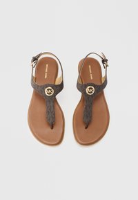 Hnědé žabky s tmavě vzorovaným svrškem, zlatým logem a plochou gumovou podrážkou. Součástí je nastavovací popruh kolem kotníku.