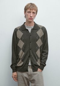 Donkergrijze cardigan met een ruitpatroon in lichtbruin en crème, met een kraag en knopen, gedragen over een grijs shirt.