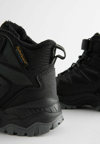 Zwarte wandelschoenen van synthetisch materiaal met textuur, zachte voering, opvallende traction-zolen en HydroGuard-merk op de zijkant.