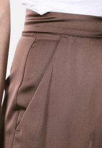 Gonna marrone a vita alta in tessuto liscio, con pieghe sottili e un design elegante. La superficie ha una texture morbida e opaca.