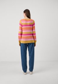 Striped sweater with knit texture in pink, yellow, and orange. Long sleeves, round neckline, paired with blue baggy jeans and light-colored shoes.