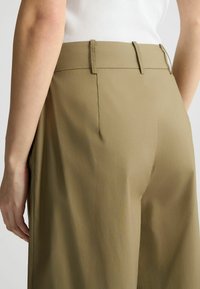Pantaloni khaki realizzati in un tessuto leggero, con vita media, due tasche posteriori e una texture liscia con sottili dettagli di cucitura.
