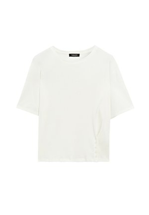 Frau läuft und trägt ein weißes T-Shirt, dunkle weite Hose, schwarze Sandalen und einen rot-weiß gestreiften Pullover, der um die Taille gebunden ist.