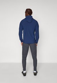 Marineblå sweater med høj krave og lange ærmer, parret med mørkegrå bukser. Bukserne har en let tætsiddende pasform og sidelommer.