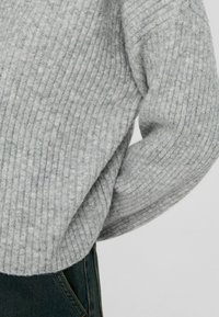 Pull gris côtelé avec un tissu doux et texturé. Présente une coupe ample, des épaules tombantes et un ourlet raccourci, associé à un jean foncé.