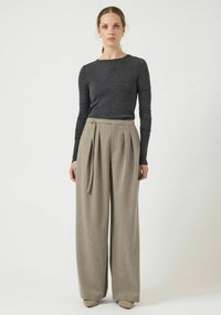 Top grigio a maniche lunghe abbinato a pantaloni beige a vita alta, a gamba larga, con pieghe e fiocco laterale, impreziositi da una chiusura con bottoni.