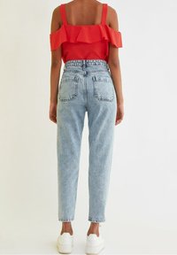 Czerwony top z odkrytymi ramionami z falbaną, zestawiony z jasnoniebieskimi jeansami z wysokim stanem o luźnym kroju i tylnymi kieszeniami. Białe trampki.