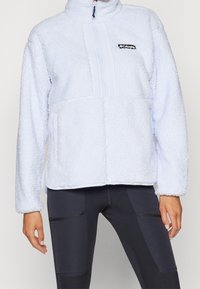 Light blue fleece pullover with a high collar, zippered front, two side pockets, textured fabric, and a black Columbia logo patch.