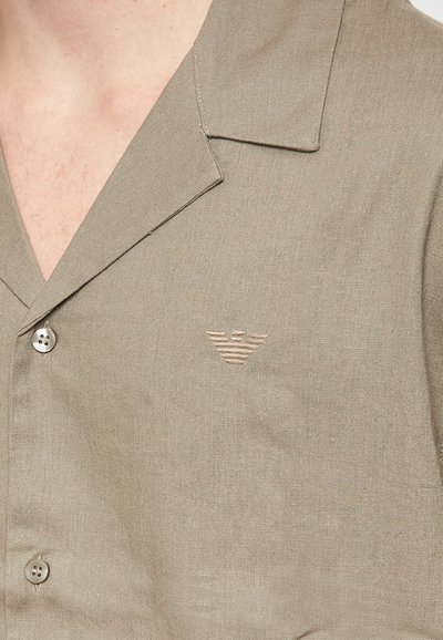 Beige kortærmet skjorte i et let materiale, med en skarp krave, to knapper og et diskret broderet logo på brystet.