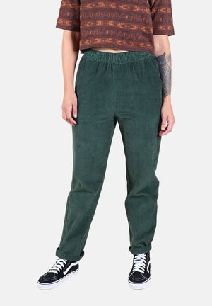Pantalon en velours côtelé vert à coupe décontractée, doté d'une ceinture élastique et de rayures texturées. Associé à des baskets noires à lacets.