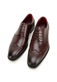 Hnědé kožené společenské boty s hladkým povrchem, s designem wingtip, šesti očky a kontrastním červeným interiérem.