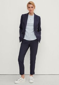 Blazer blu navy e pantaloni abbinati, abbinati a una blusa a righe azzurre e sneakers bianche con due fasce. Vestibilità su misura e texture liscia.