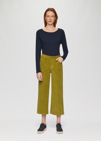 Marineblaues Langarmoberteil mit weitem Rundhalsausschnitt, kombiniert mit hochgeschnittenen, weit geschnittenen olivgrünen Cordhosen und schwarzen Sneakers mit Plateau.