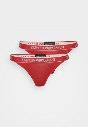 String rouge en coton avec une large ceinture élastique blanche arborant le logo et la marque "EMPORIO ARMANI". Texture lisse, design minimaliste.