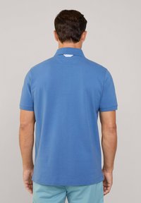 Niebieska koszulka polo z miękkiego, teksturowanego materiału, z klasycznym kołnierzykiem, krótkimi rękawami i prostym dołem. Prosty design, bez wzorów.