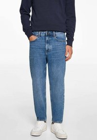 Svijetloplave traperice opuštenog kroja, s dizajnom od pet džepova i neuređenim rubovima, u kombinaciji s bijelim tenisicama i tamnom duksericom.