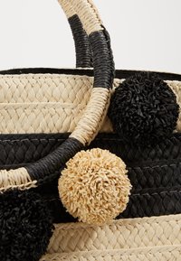 Borsa tote rotonda in paglia intrecciata con sezioni alternate nere e naturali, con pompon testurizzati neri e beige attaccati al manico.