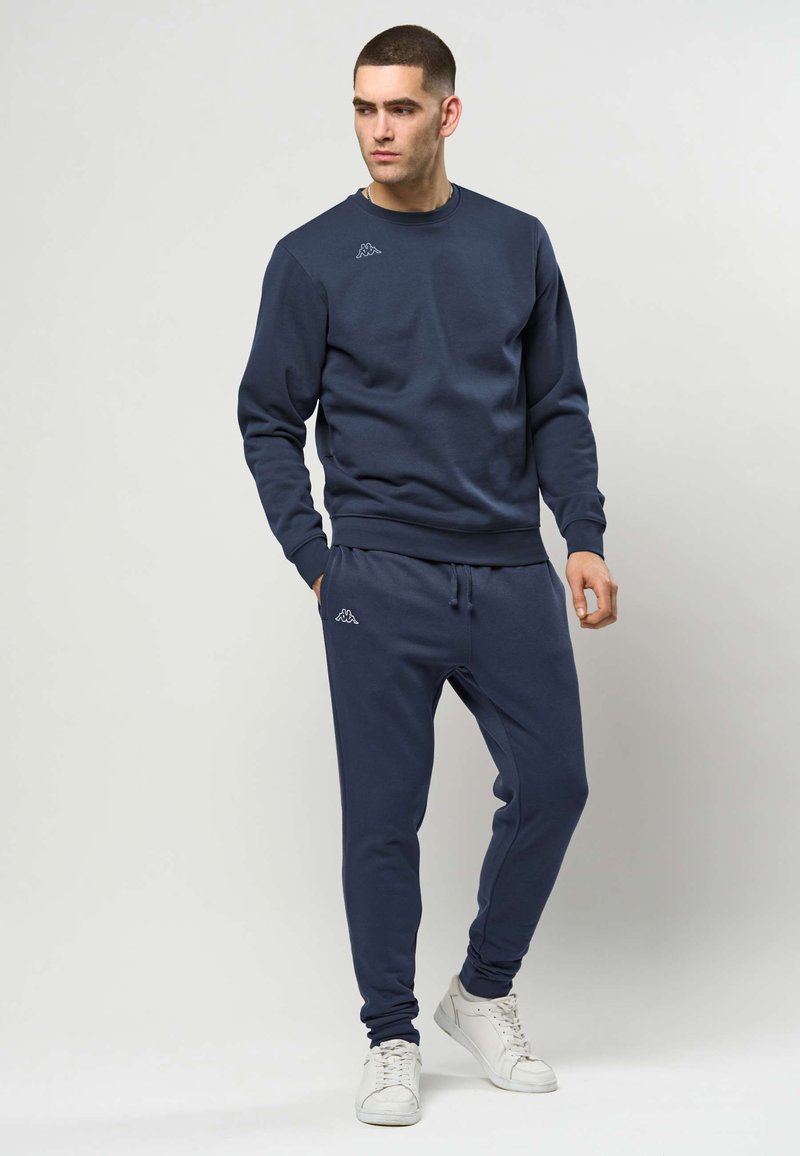 Marineblå genser og joggebukse i myk bomull, med ribbestrikkede mansjetter, snøring i livet, og en liten logo på hver del.