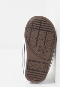 Podeszwa sneakersów Converse All Star, brązowy materiał gumowy z wzorem gripu, czarno-biała lamówka wzdłuż brzegów, smukły i zaokrąglony kształt.