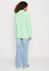 Mintgrønn blazer med skreddersydd passform, notched revers og knapper på mansjettene, kombinert med løse lys blå denimbukser og hvite sneakers.